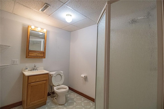 bathroom featuring a drop ceiling, vanity, a shower with shower door, and toilet