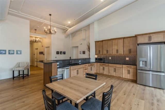 kitchen with pendant lighting, stainless steel appliances, a peninsula, dark countertops, and an inviting chandelier