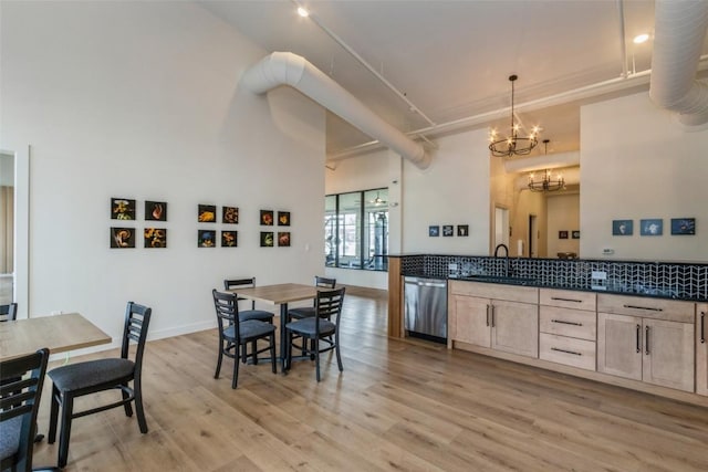 kitchen featuring dark countertops, decorative light fixtures, light brown cabinetry, stainless steel dishwasher, and a sink