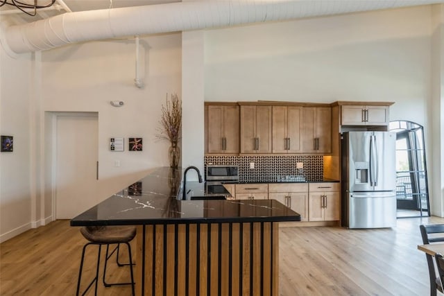 kitchen with light wood finished floors, dark countertops, a breakfast bar, stainless steel appliances, and backsplash