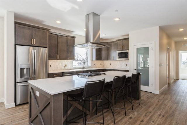 kitchen featuring light countertops, appliances with stainless steel finishes, a center island, and island range hood