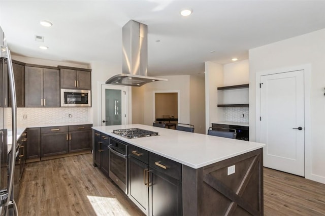 kitchen featuring island exhaust hood, stainless steel appliances, light countertops, a kitchen island, and dark brown cabinets