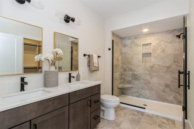 full bath featuring double vanity, a walk in closet, a sink, and tiled shower