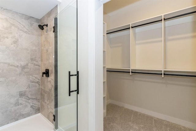 bathroom with a spacious closet, a shower stall, and baseboards