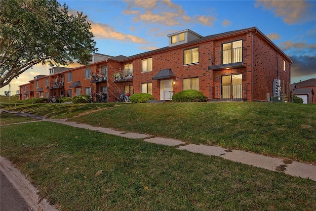 view of property featuring brick siding, a lawn, and central air condition unit