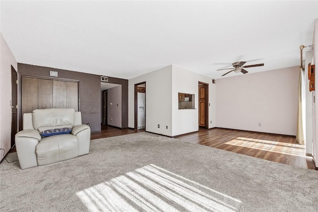 unfurnished living room with a ceiling fan, carpet flooring, baseboards, and wood finished floors