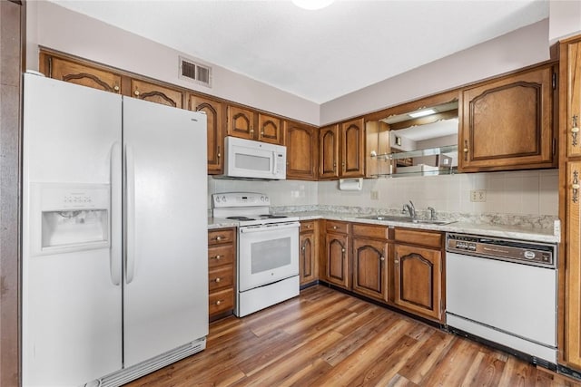 kitchen with white appliances, a sink, light countertops, light wood finished floors, and brown cabinetry