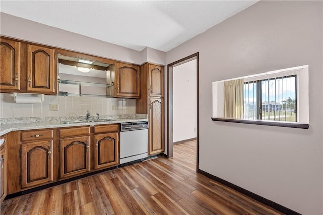 kitchen with dark wood-style floors, decorative backsplash, brown cabinetry, white dishwasher, and a sink