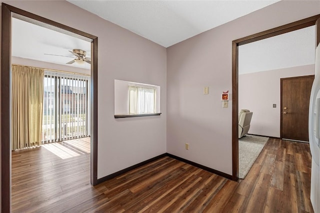 unfurnished room with dark wood-style floors, a ceiling fan, and baseboards