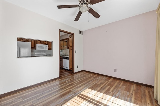 spare room with baseboards, visible vents, a ceiling fan, wood finished floors, and a sink