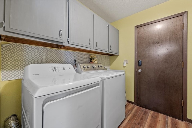 clothes washing area with washing machine and clothes dryer, cabinet space, a textured ceiling, wood finished floors, and baseboards