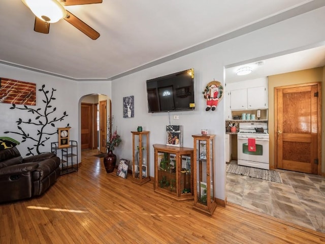 living area with light wood-type flooring, arched walkways, and ceiling fan