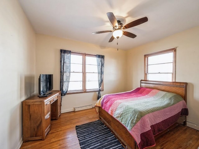 bedroom featuring baseboards, multiple windows, baseboard heating, and wood finished floors