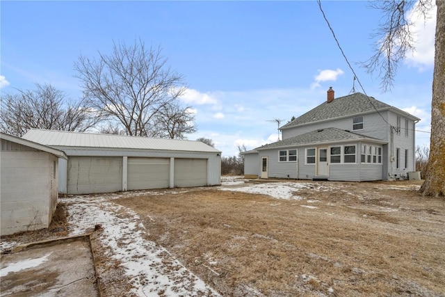 snow covered rear of property featuring a garage and an outbuilding