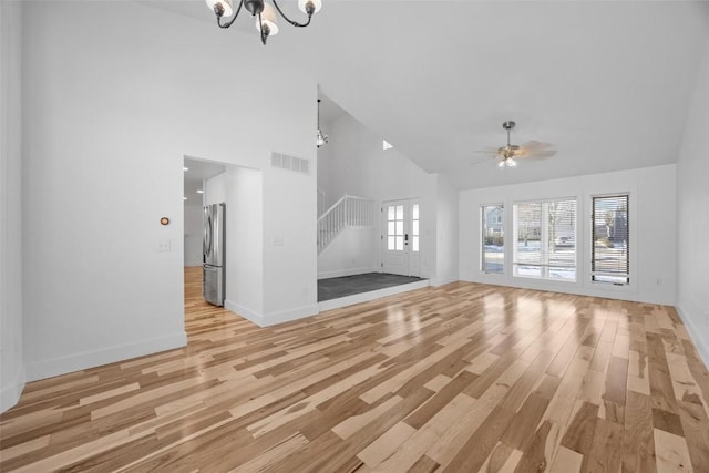 unfurnished living room featuring ceiling fan with notable chandelier, light wood-type flooring, and high vaulted ceiling