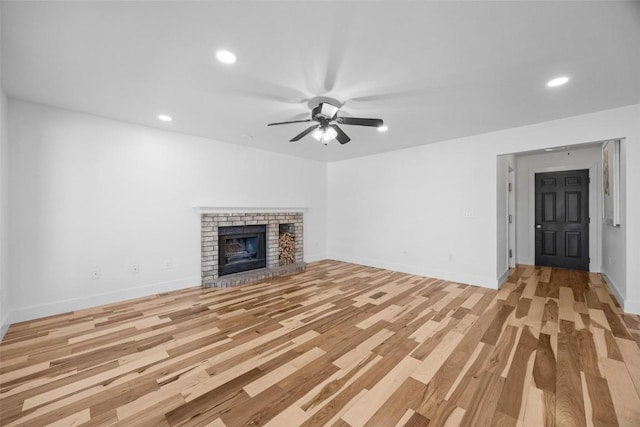 unfurnished living room with a brick fireplace, ceiling fan, and light wood-type flooring