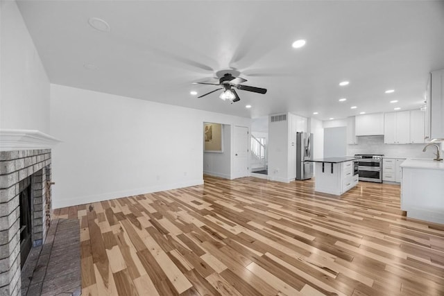 unfurnished living room featuring ceiling fan, sink, light hardwood / wood-style flooring, and a brick fireplace