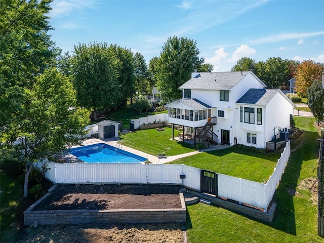 rear view of property featuring a yard, a fenced in pool, a shed, and a sunroom