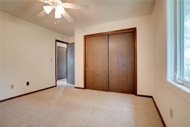 unfurnished bedroom with a textured ceiling, ceiling fan, light carpet, and a closet