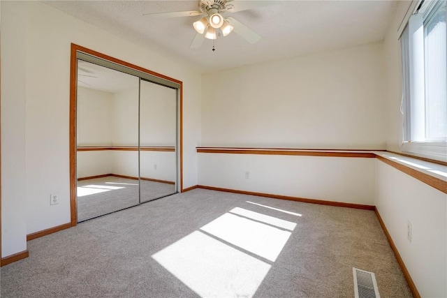 unfurnished bedroom featuring multiple windows, light colored carpet, a closet, and ceiling fan