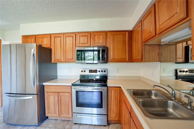 kitchen with light tile patterned flooring, a textured ceiling, stainless steel appliances, and sink