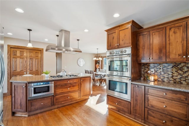 kitchen with decorative backsplash, decorative light fixtures, light hardwood / wood-style floors, island exhaust hood, and stainless steel appliances