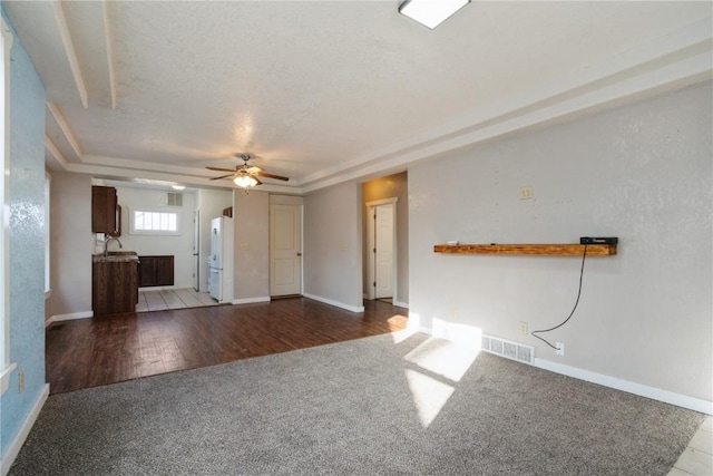 unfurnished living room with a tray ceiling, ceiling fan, sink, and carpet flooring