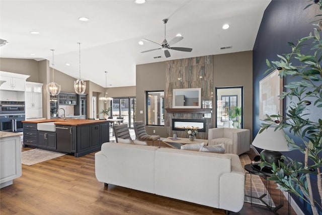 living room featuring sink, high vaulted ceiling, hardwood / wood-style floors, a fireplace, and ceiling fan with notable chandelier