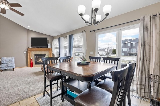 carpeted dining space with ceiling fan with notable chandelier, vaulted ceiling, and a tiled fireplace