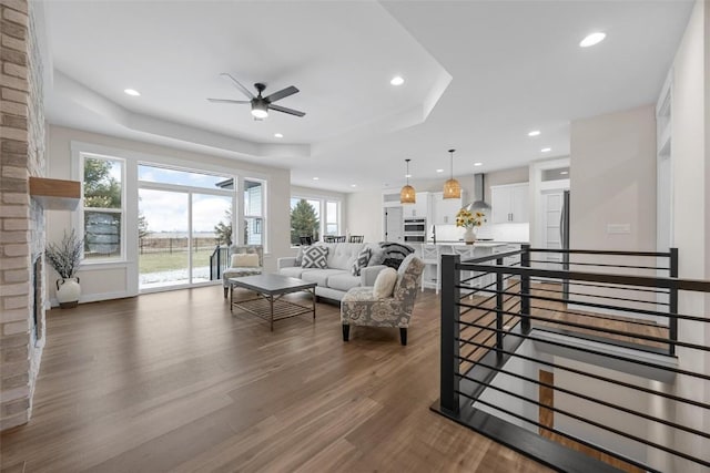 living room featuring a raised ceiling, a wealth of natural light, dark hardwood / wood-style flooring, and ceiling fan