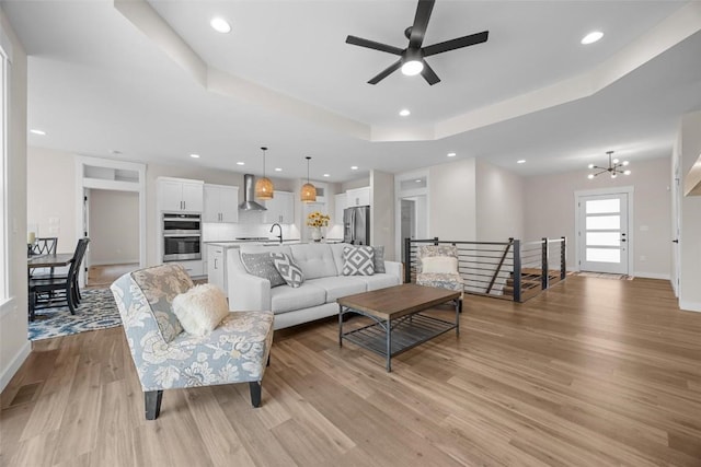 living room featuring a tray ceiling, light hardwood / wood-style flooring, and ceiling fan with notable chandelier