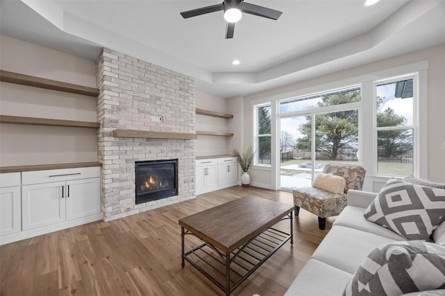 living room with a fireplace, a tray ceiling, and light hardwood / wood-style flooring