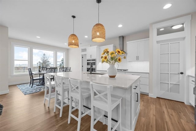 kitchen featuring white cabinets, an island with sink, hanging light fixtures, and tasteful backsplash