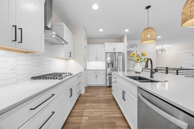 kitchen featuring backsplash, white cabinets, wall chimney range hood, sink, and appliances with stainless steel finishes