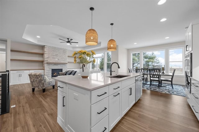 kitchen with sink, a center island with sink, dishwasher, a fireplace, and white cabinetry