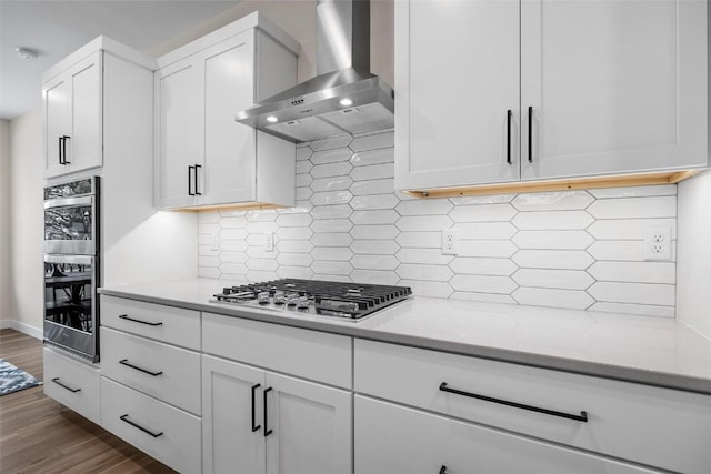 kitchen featuring decorative backsplash, light stone countertops, wall chimney exhaust hood, stainless steel appliances, and white cabinetry