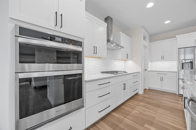 kitchen with backsplash, white cabinets, wall chimney range hood, and stainless steel appliances