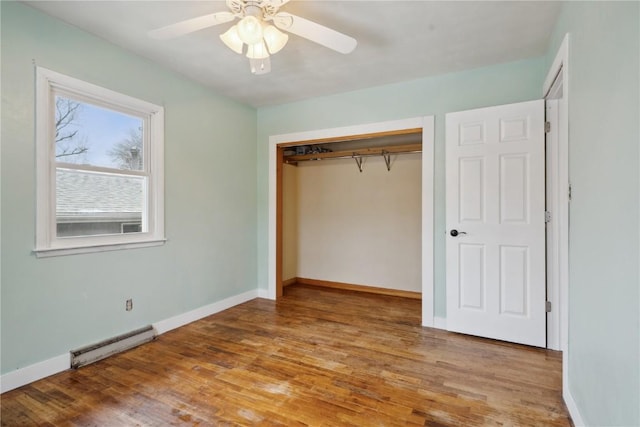 unfurnished bedroom featuring ceiling fan, a closet, hardwood / wood-style floors, and a baseboard heating unit