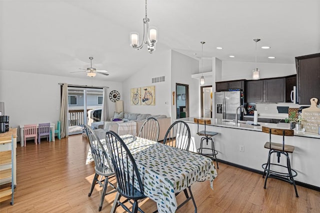 dining space with ceiling fan with notable chandelier, light hardwood / wood-style flooring, lofted ceiling, and sink