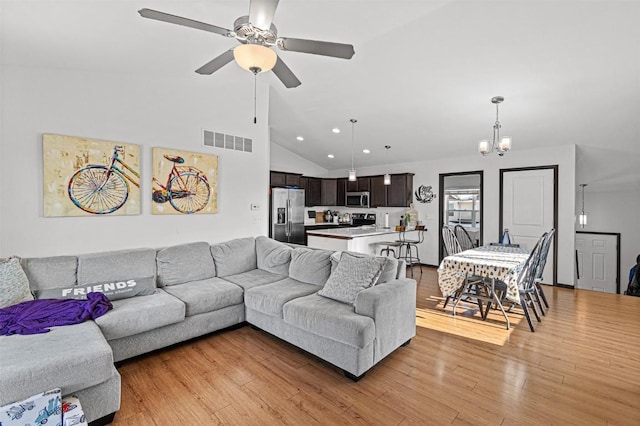 living room featuring ceiling fan with notable chandelier, vaulted ceiling, and light wood-type flooring