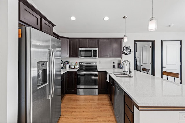 kitchen with appliances with stainless steel finishes, light wood-type flooring, dark brown cabinetry, sink, and pendant lighting