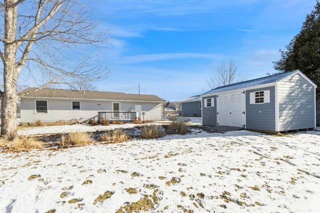 snow covered back of property with an outdoor structure and a deck