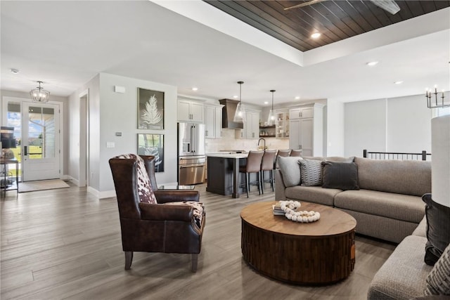 living room with a raised ceiling, hardwood / wood-style flooring, sink, and an inviting chandelier