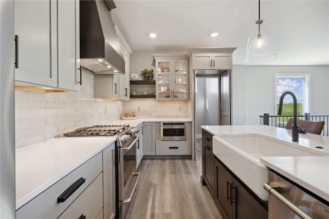 kitchen with decorative backsplash, stainless steel appliances, sink, wall chimney range hood, and pendant lighting