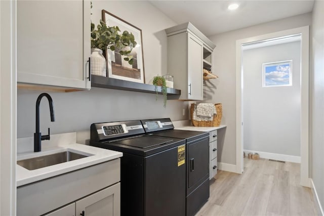 washroom featuring washing machine and clothes dryer, sink, cabinets, and light wood-type flooring