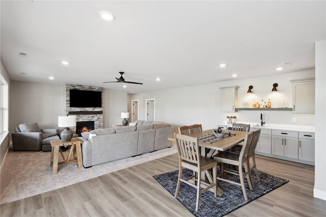 dining room featuring ceiling fan, sink, light wood-type flooring, and a fireplace