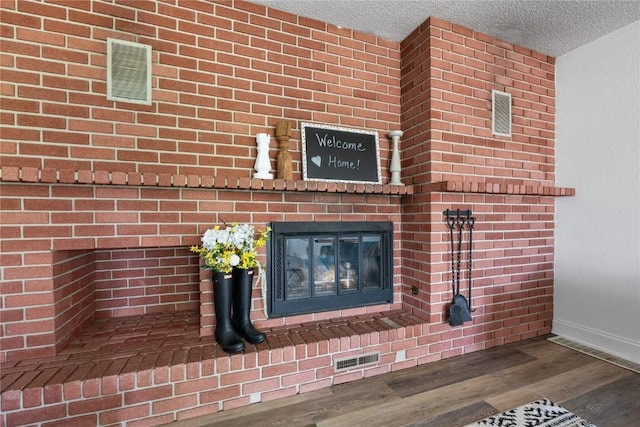 interior details with wood-type flooring, a brick fireplace, and a textured ceiling