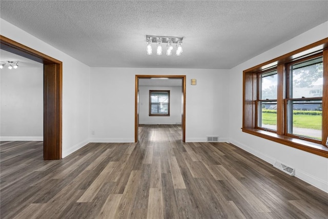 unfurnished dining area featuring rail lighting, a textured ceiling, and dark hardwood / wood-style floors