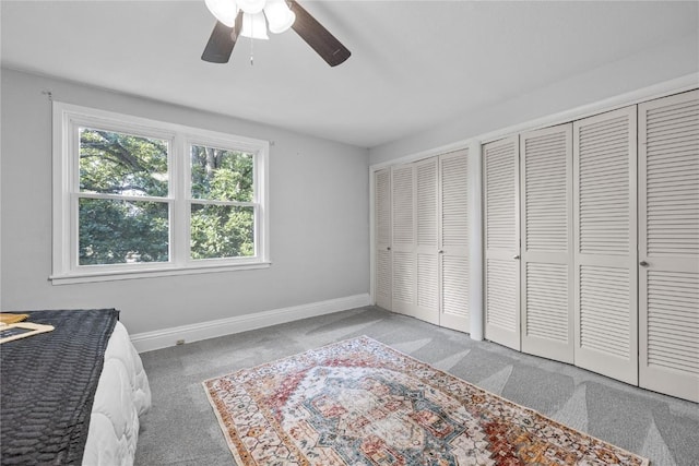 unfurnished bedroom featuring ceiling fan, carpet, and multiple closets