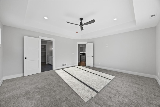 unfurnished bedroom featuring ensuite bathroom, a raised ceiling, ceiling fan, and carpet flooring